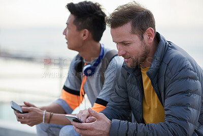 Buy stock photo Hangout, phone and typing with men at beach together for bonding, browsing or social media. App, internet and text message with male best friends outdoor in nature for break, communication or relax