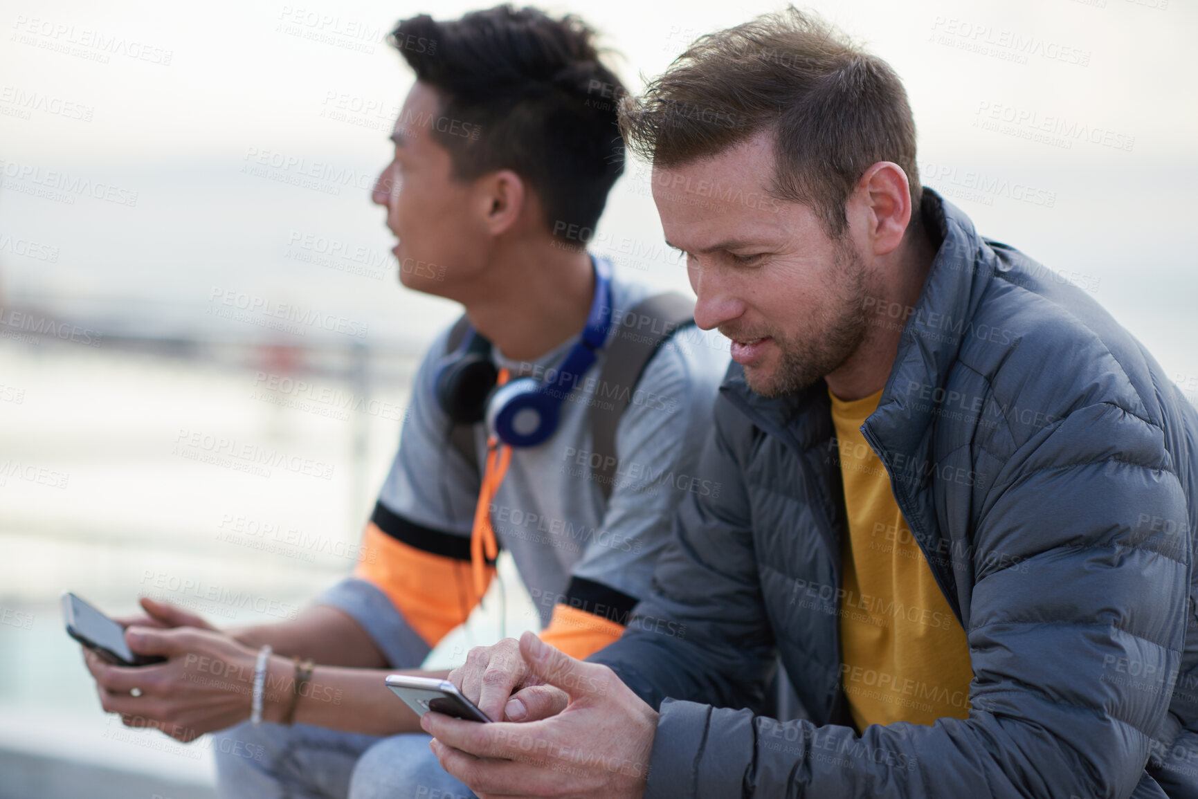 Buy stock photo Hangout, phone and typing with men at beach together for bonding, browsing or social media. App, internet and text message with male best friends outdoor in nature for break, communication or relax
