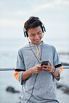 Young asian man using smartphone listening to music wearing headphones by the beach