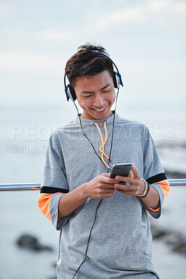 Buy stock photo Fitness, music and phone with Asian man at beach for health, playlist streaming or update. App, audio and headphones with runner typing on mobile for improvement, performance or progress tracking