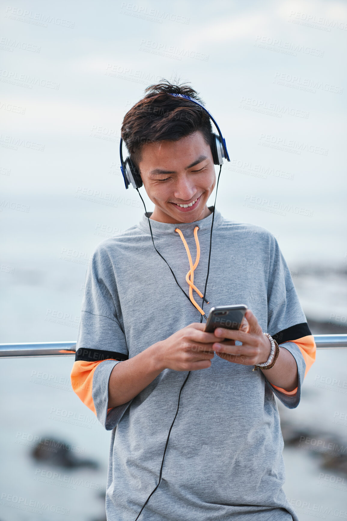 Buy stock photo Fitness, music and phone with Asian man at beach for health, playlist streaming or update. App, audio and headphones with runner typing on mobile for improvement, performance or progress tracking