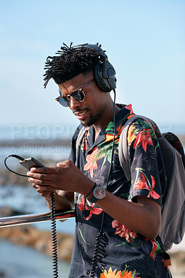 Buy stock photo Phone, headphones and black man by beach on holiday for texting, social media or contact on mobile app. Audio tech, promenade and person on cellphone for blog on vacation tips by ocean with music.