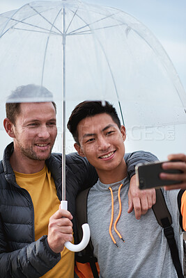 Buy stock photo Selfie, smile or friends outdoor with umbrella, hangout picture or bonding post on winter trip. Happy, digital or men with rain shield, holiday connection or memory capture for social media update.