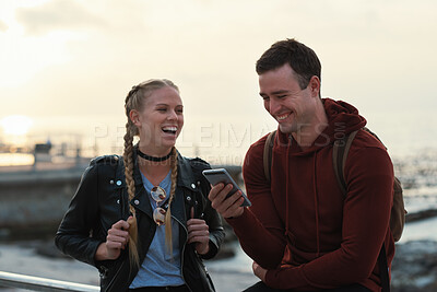 Buy stock photo Phone, friends and laugh by sea with social media, funny joke and text message with meme on vacation. Happy people, mobile and students at beach for humor, post or gossip at sunset on holiday break