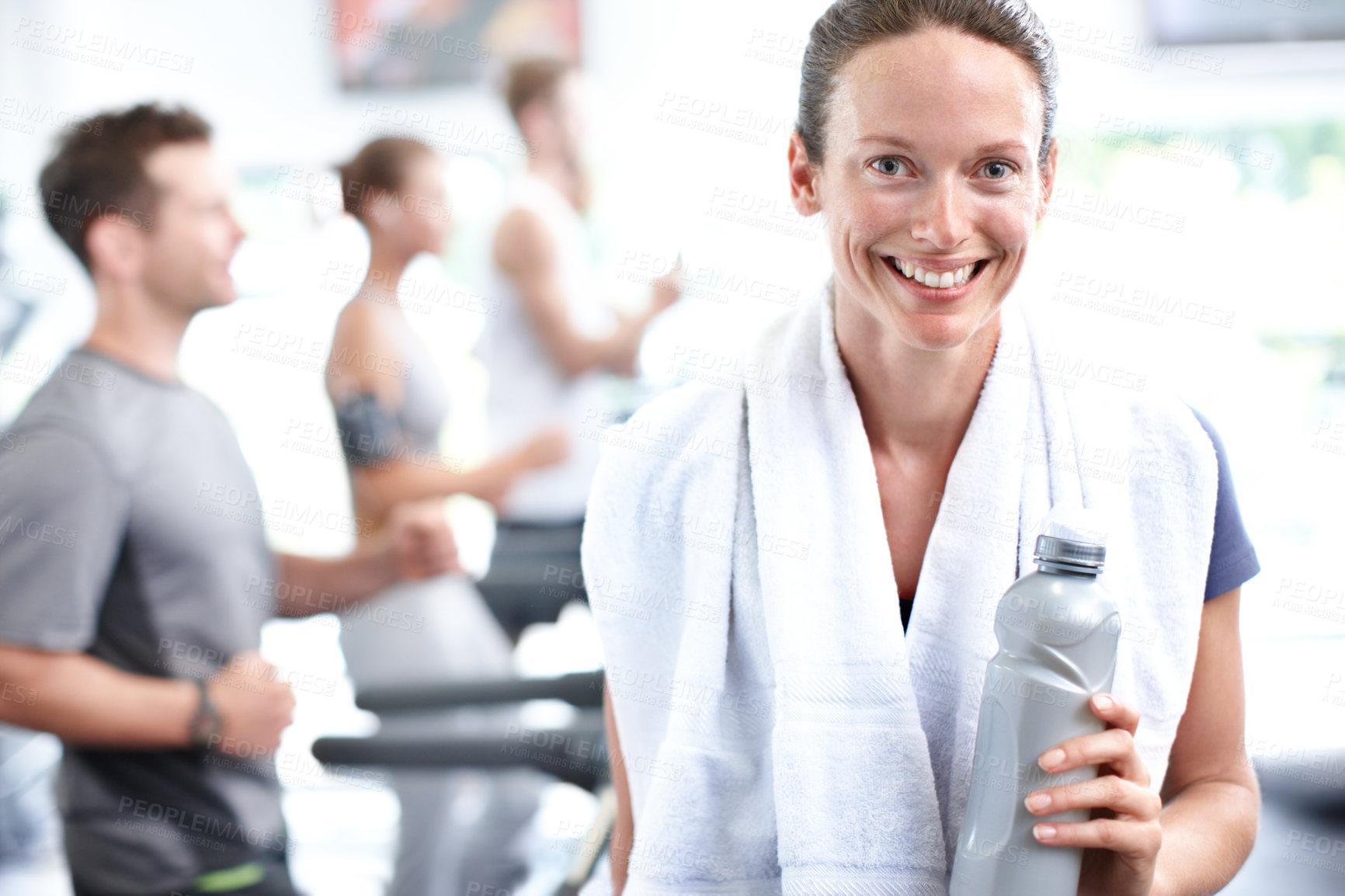 Buy stock photo Shot of a young woman in sportswear with men and women joggin on treadmills in the background