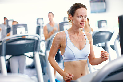 Buy stock photo Shot of a young woman jogging on a treadmill in a gym
