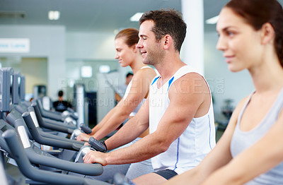 Buy stock photo Shot of young men and women cycling on exercise bikes in a gym