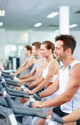 Buy stock photo Shot of young men and women cycling on exercise bikes in a gym