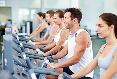 Buy stock photo Shot of young men and women cycling on exercise bikes in a gym