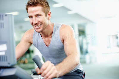 Buy stock photo Shot of a young man on a cycling machine in a gym