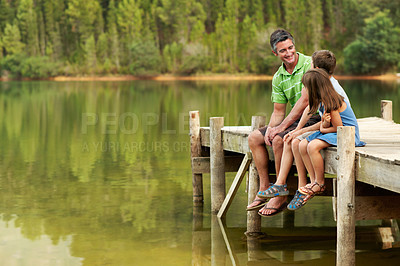 Buy stock photo Smile, father and relax with children at lake, conversation or bonding together on holiday. Space, man and talk on pier with kids, family connection and weekend break on vacation trip in countryside