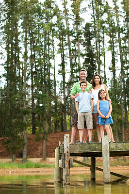 Buy stock photo Portrait, family and happy outdoor by lake for summer holiday, vacation and together. Low angle, pier and smile of man, woman and children in nature to relax, bonding and connection or love and care