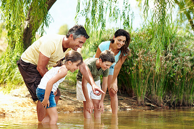 Buy stock photo Smile, parents and pointing with children at lake, adventure and discover fish on holiday. Happy, people and hand gesture in nature with kids, wildlife observation and water for sightseeing vacation