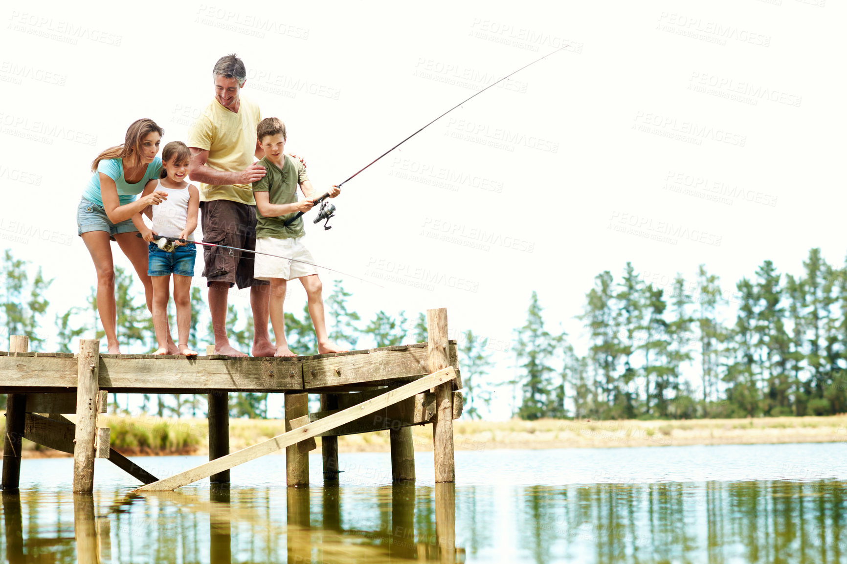 Buy stock photo Happy, parents and kids by lake for fishing, summer vacation and bonding on weekend getaway. Family, space and pier with mom, dad and children for fun, adventure and learning to catch fish together