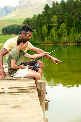 Buy stock photo Dad, tips and fishing with teenager, lake and bonding with son on vacation and connection in nature. Family, hobby and happy man with rod to catch fish in water, point and advice for boy and lesson