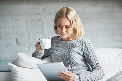 Buy stock photo A pretty young woman using a digital tablet while enjoying a cup of coffee