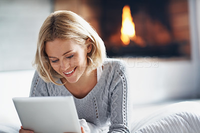 Buy stock photo A candid shot of a young woman using a digital tablet while sitting on her couch
