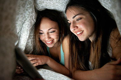 Buy stock photo Shot of two teenage girls under a blanket looking at a digital tablet
