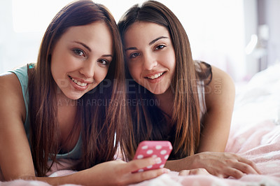 Buy stock photo Portrait of two teenage girls lying on a bed looking at a mobile phone with copyspace