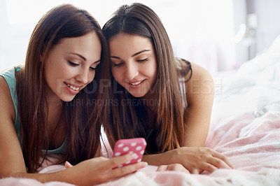 Buy stock photo Shot of two teenage girls lying on a bed looking at a cell phone with copyspace