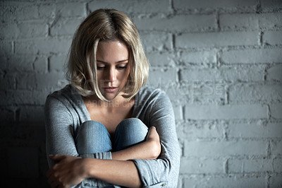 Buy stock photo A pretty young blonde woman sitting down while looking severely depressed