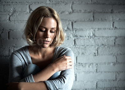 Buy stock photo A pretty young blonde woman sitting down while looking severely depressed