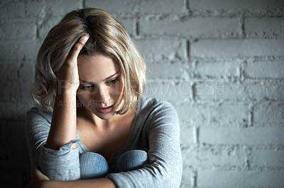 Buy stock photo A pretty young blonde woman sitting down while looking severely depressed