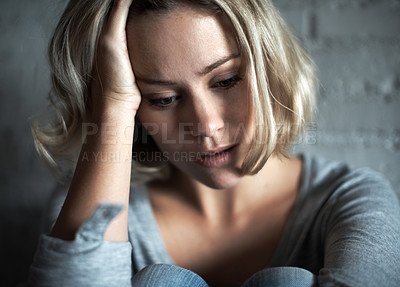 Buy stock photo A pretty young blonde woman sitting down while looking severely depressed