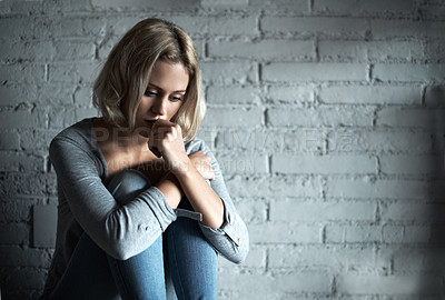Buy stock photo A pretty young blonde woman sitting down while looking severely depressed