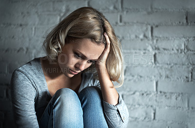 Buy stock photo A pretty young blonde woman sitting down while looking severely depressed