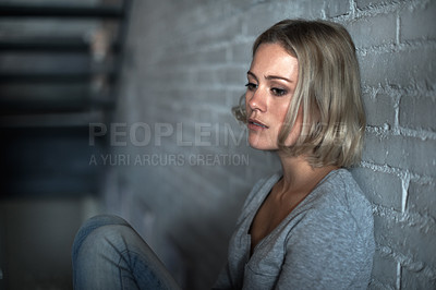 Buy stock photo A pretty young blonde woman sitting down while looking severely depressed