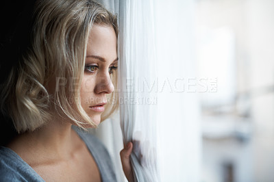 Buy stock photo A beautiful young blonde woman looking out of her window sadly