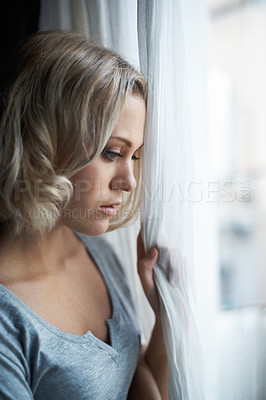Buy stock photo A beautiful young blonde woman looking out of her window sadly