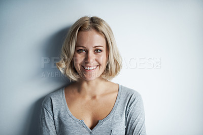 Buy stock photo Portrait of a pretty young blonde woman leaning against a white wall