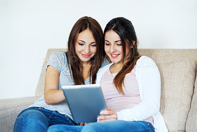 Buy stock photo Two teenage girls sharing a digital tablet while sitting on the sofa at home