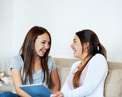 Buy stock photo Two teenage girls sharing a tablet while sitting on the sofa at home
