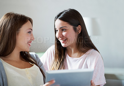 Buy stock photo Two sisters talking while holding a digital tablet