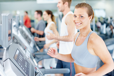 Buy stock photo Smiling young woman running on a treadmill at her local gym