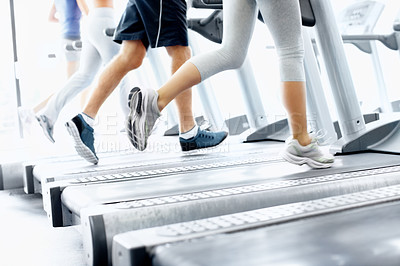 Buy stock photo Cropped view of young people's legs while they run on treadmills at the gym