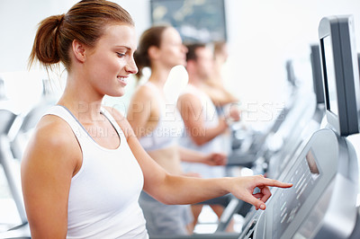 Buy stock photo Young woman selecting a speed option on a treadmill at the gym