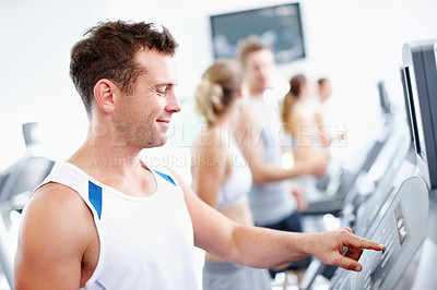 Buy stock photo Young guy selecting a speed option on a treadmill at the gym