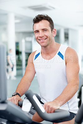 Buy stock photo Smiling young guy sitting on an exercise bicycle at the gym - portrait