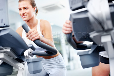 Buy stock photo Young woman using an exercise bicycle at her local gym