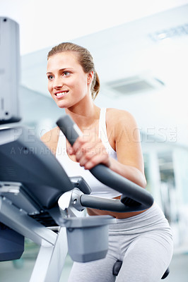 Buy stock photo Young woman using an exercise bicycle at her local gym with a smile