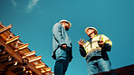 Construction, architect or talk to manager on roof for site inspection, building update or teamwork. Low angle, men and project foreman with blueprint for renovation progress, architecture and safety