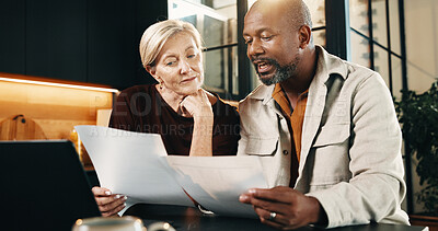 Buy stock photo Interracial couple, laptop and conversation with paperwork in home for finance, bills or investment. Mature man, woman and documents with tech for financial planning, budget expenses or invoices