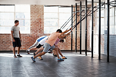 Buy stock photo Shot of a group of people using resistance bands in a crossfit class while an instructor looks on