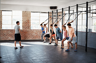 Buy stock photo Shot of a group of people using resistance bands in a crossfit class while an instructor looks on