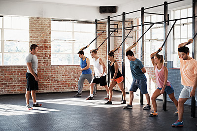 Buy stock photo Shot of a group of people using resistance bands in a crossfit class while an instructor looks on
