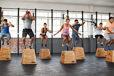 Buy stock photo Shot of a group of people jumping onto boxes in a crossfit class